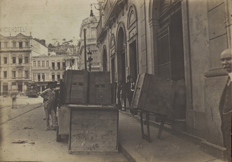A chegada do acervo da Biblioteca Nacional à atual rua do Passeio, vendo-se ao fundo um trecho do largo da Lapa que manteve seu aspecto até os dias atuais.